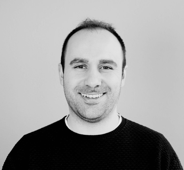 A black and white portrait of smiling Bruno Almeida, Vice President of IT operations at Fortum, wearing a black sweater.